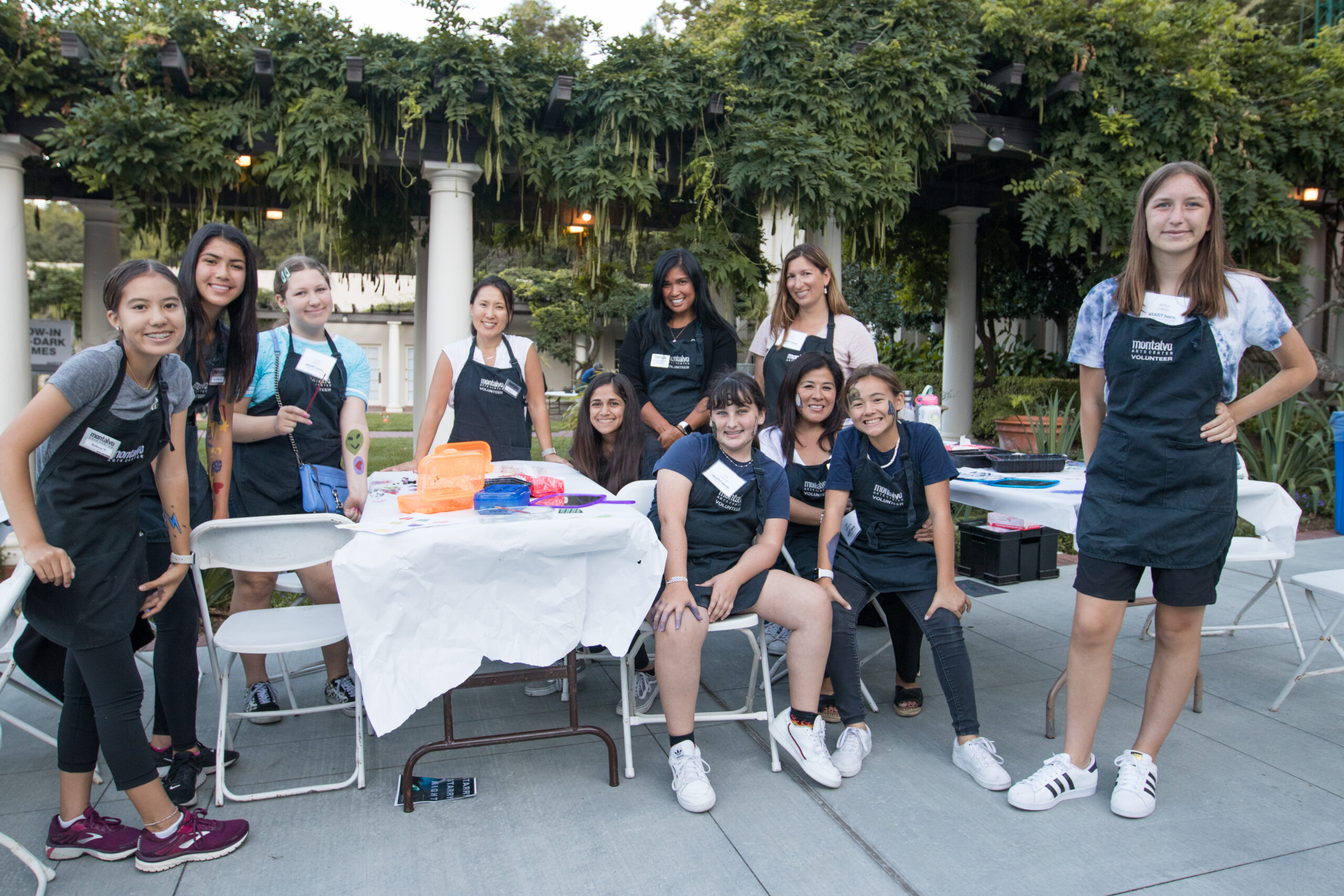 Image: A group of young women wearing black aprons reading “Montalvo Volunteers” gather in a garden